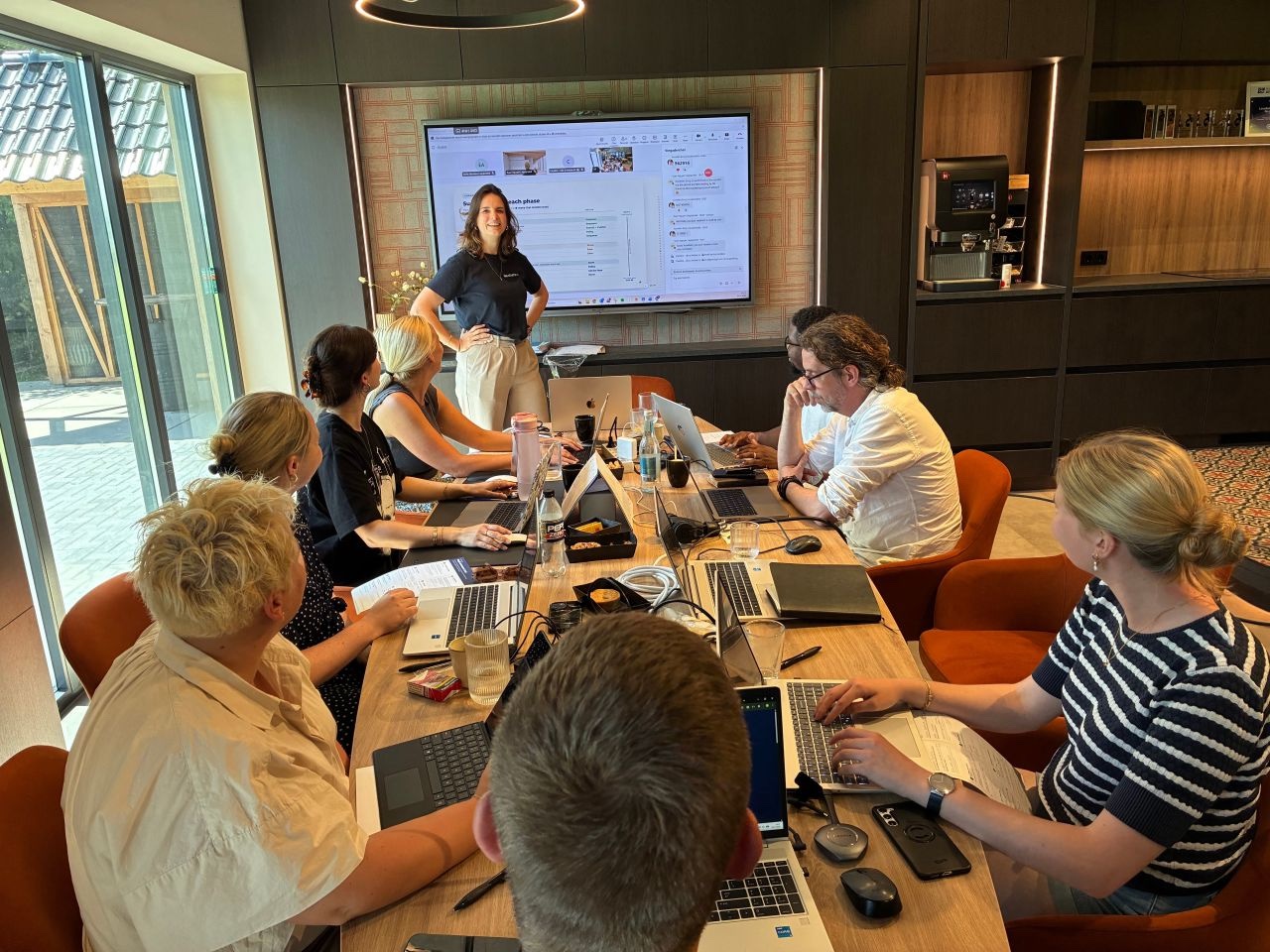 Carolina geeft training aan een team dat rond een tafel op laptops werkt